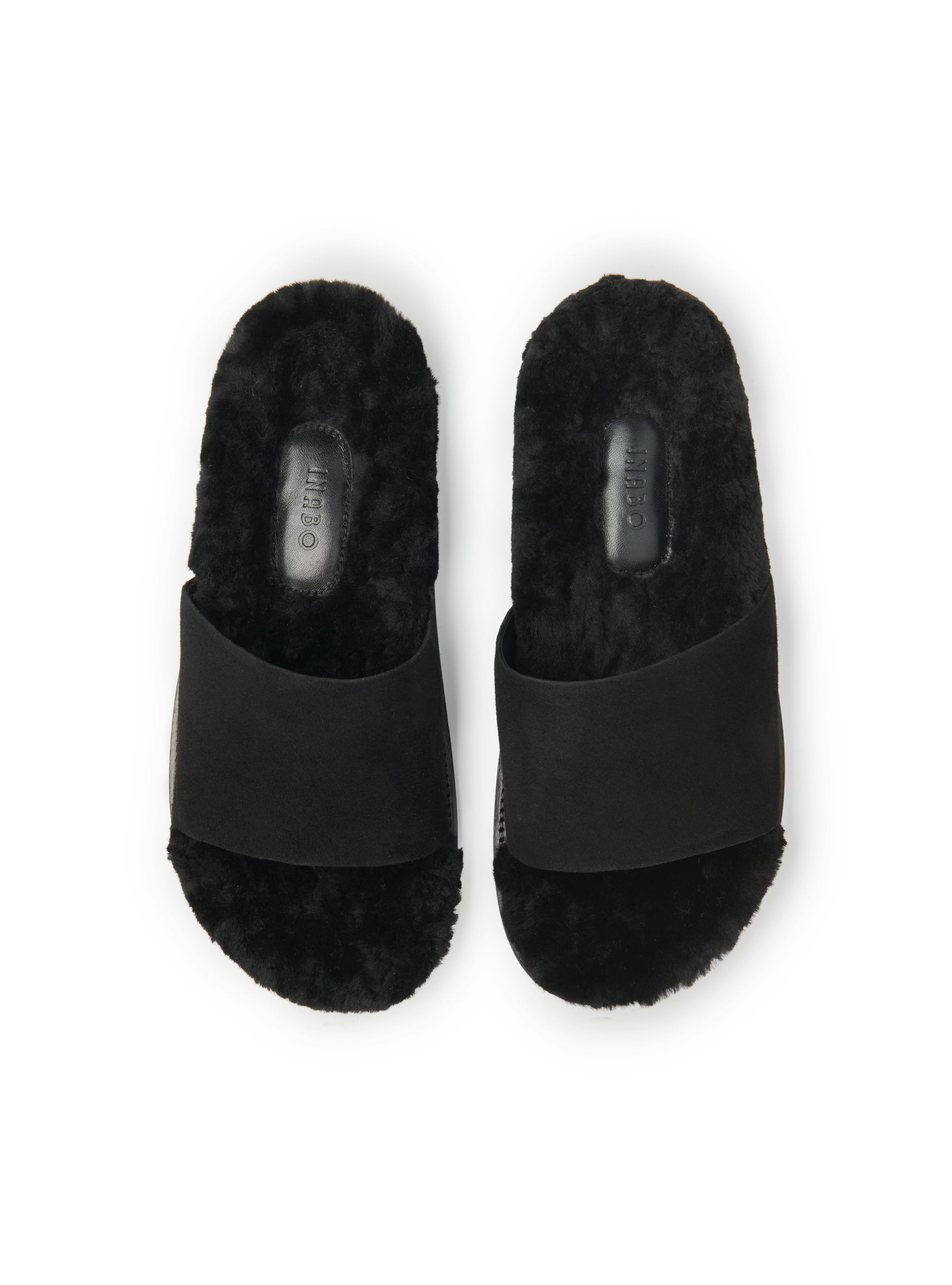 Women's pair of black shearling slip-in slippers on white background.
