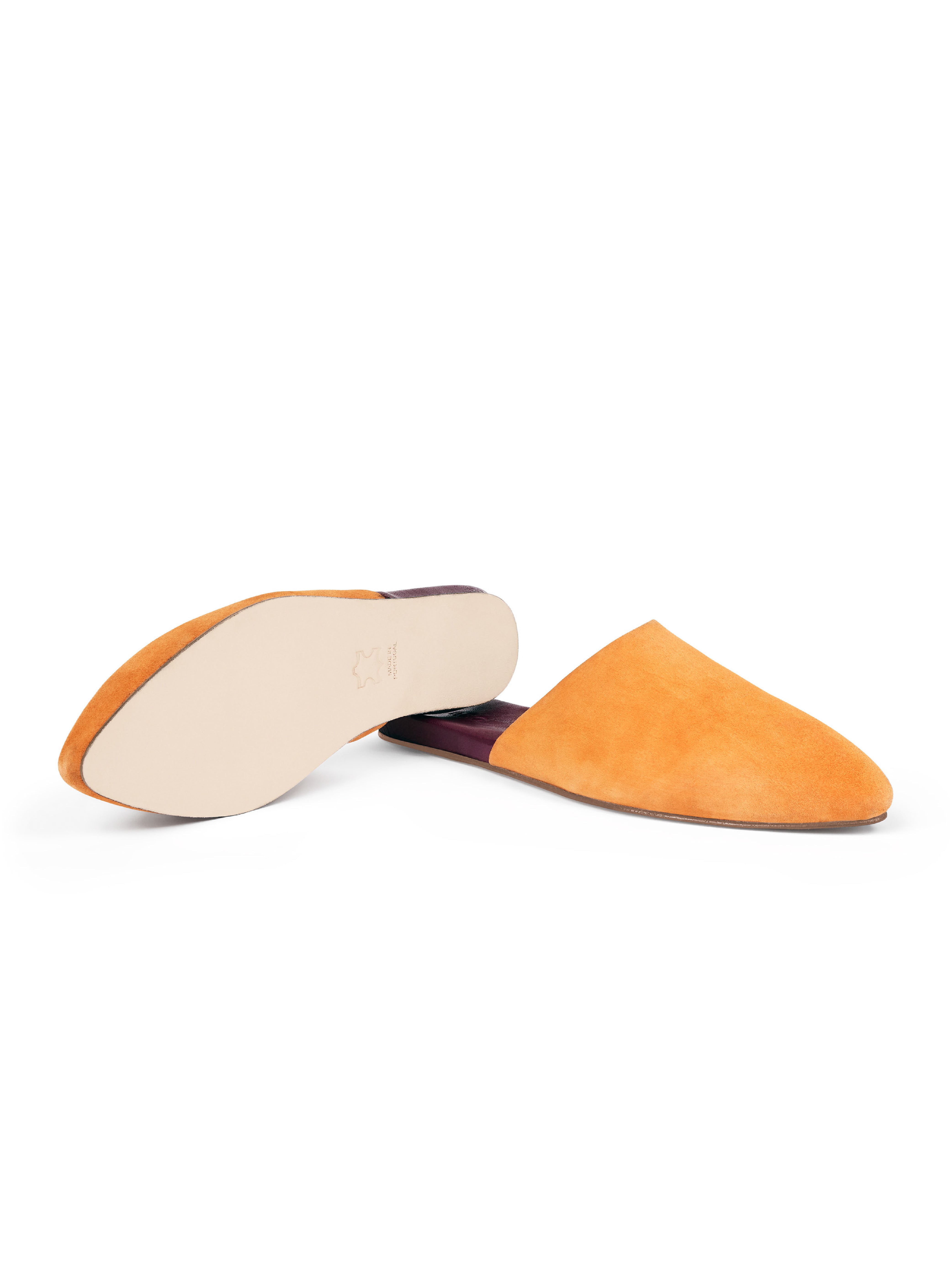 Women's pair of yellow suede pointed-toe slippers with leather outsoles on a white background