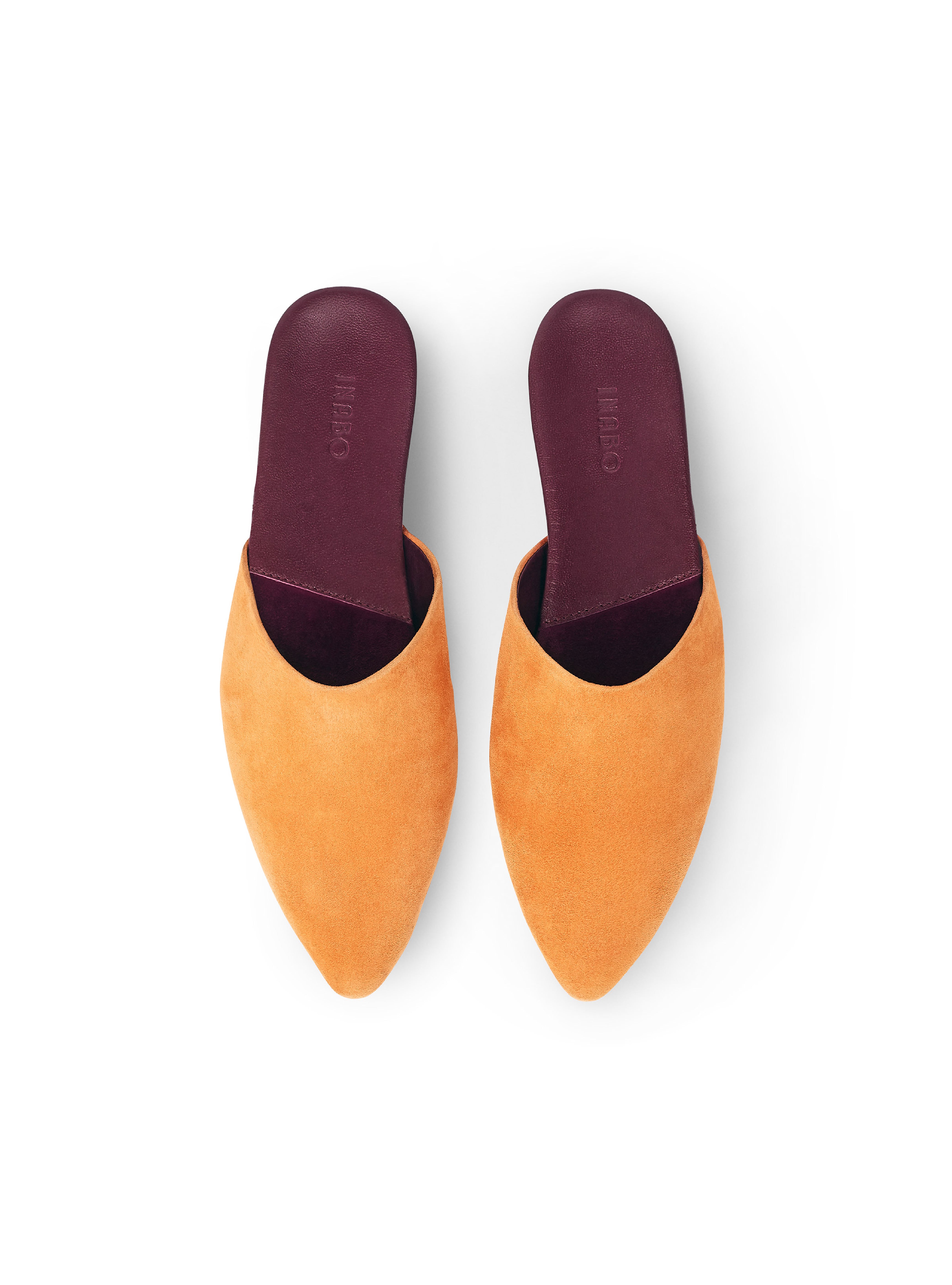 Women's pair of saffron yellow suede pointed-toe slippers with burgundy insoles on a white background