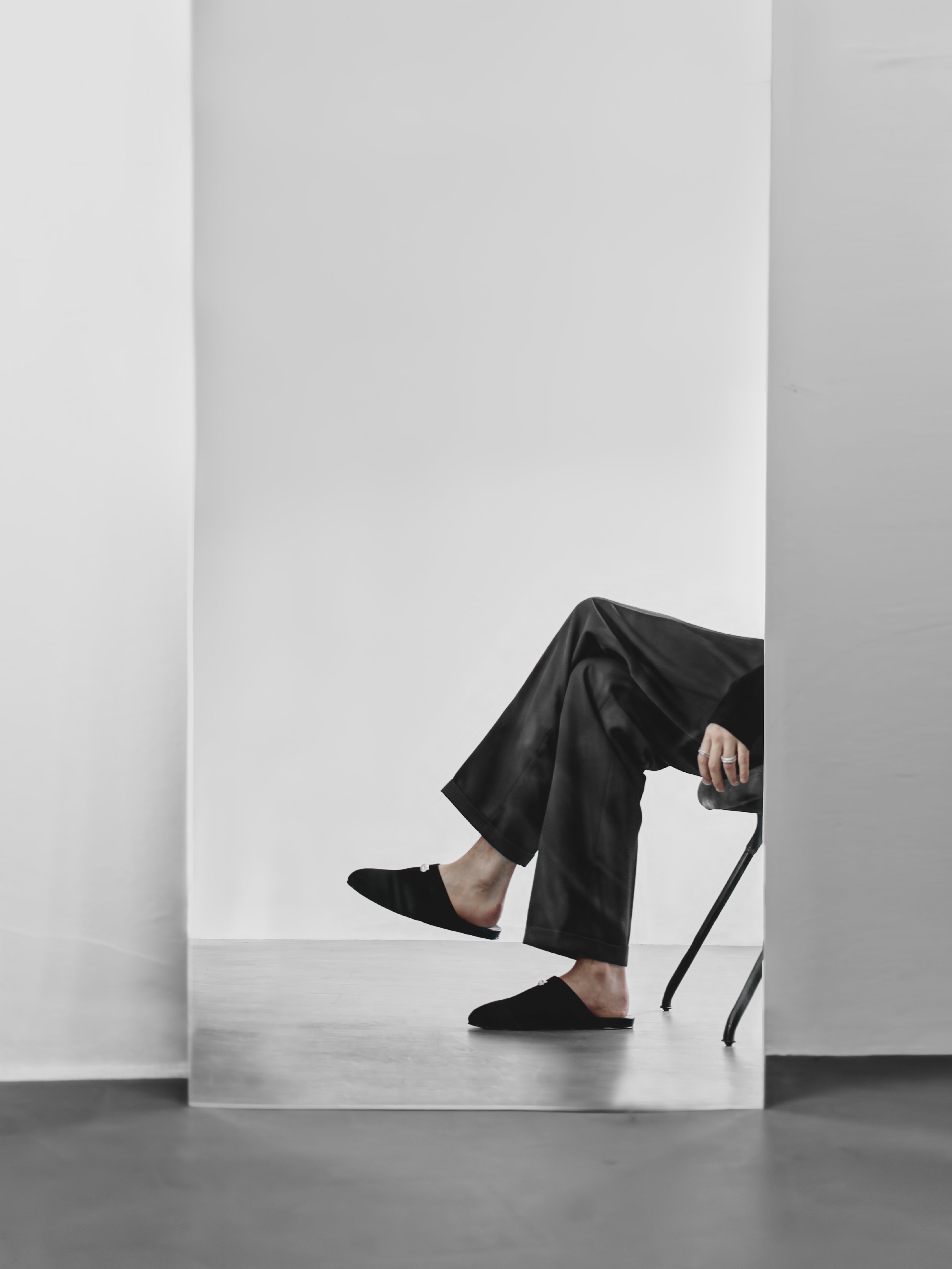 Man wearing black suede shoes and pants sitting on a chair infront of a mirror