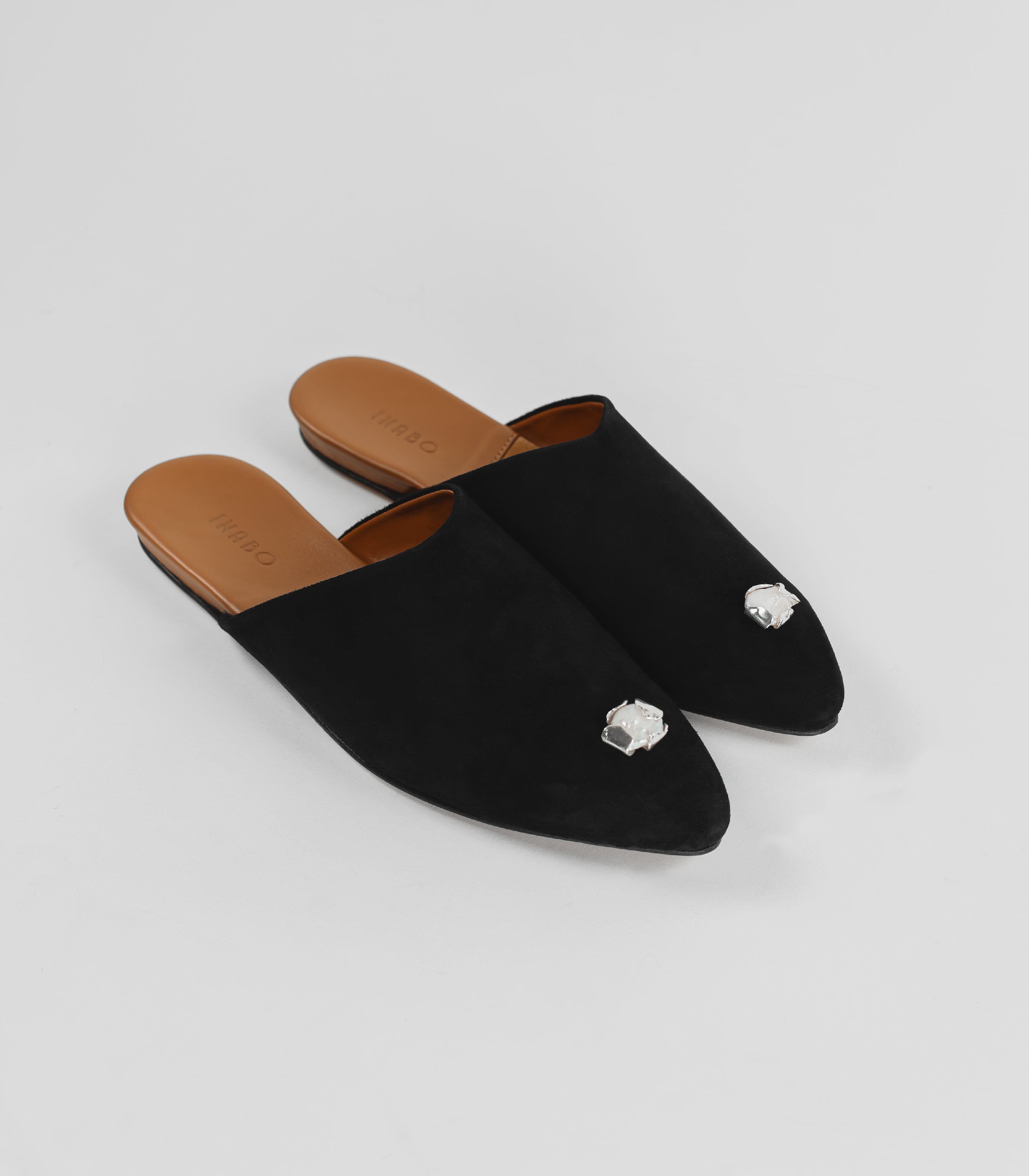 A pair of black suede slippers with a silver jewelry attached. 