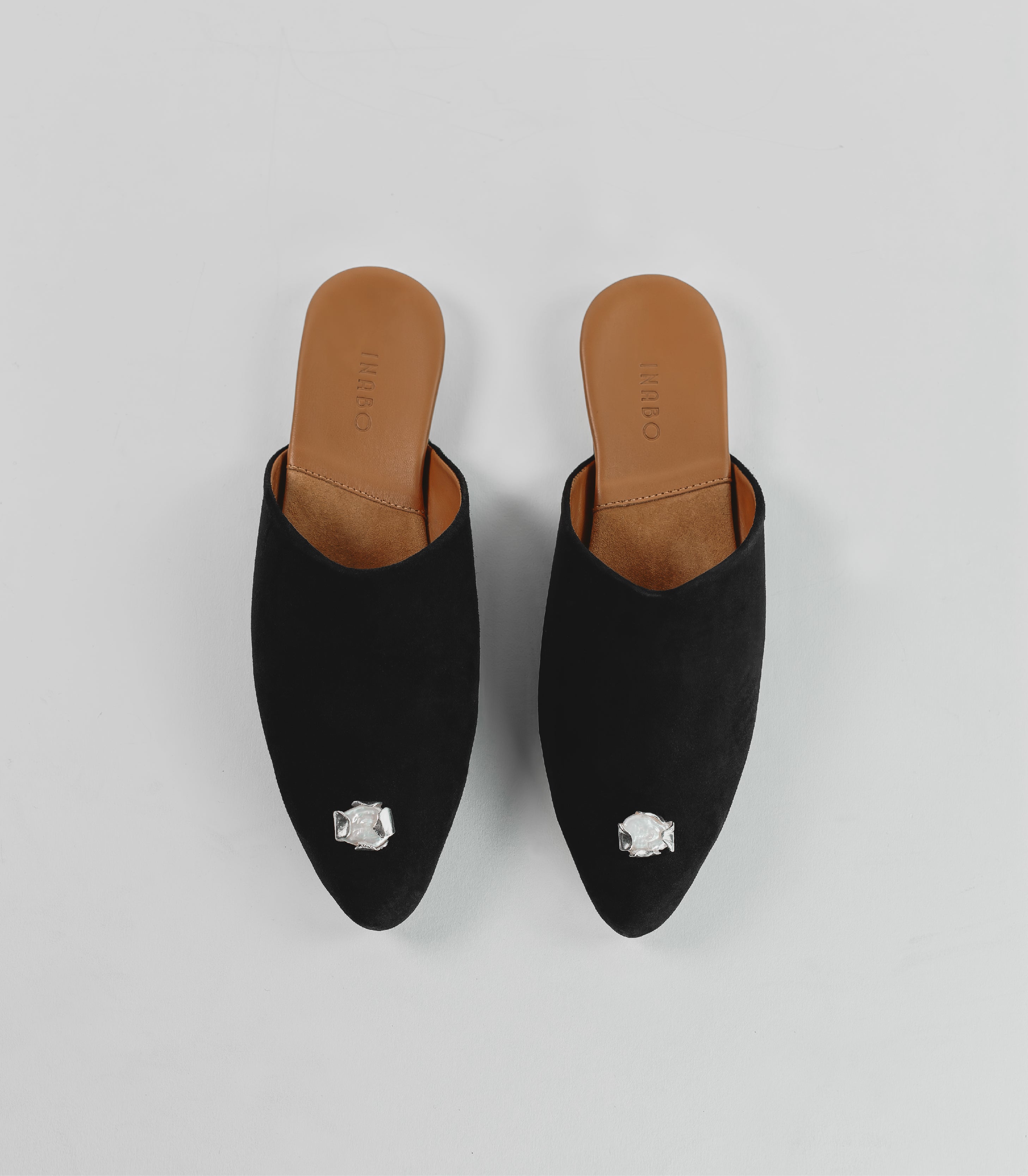 A pair of black suede slippers with a silver jewelry attached. 