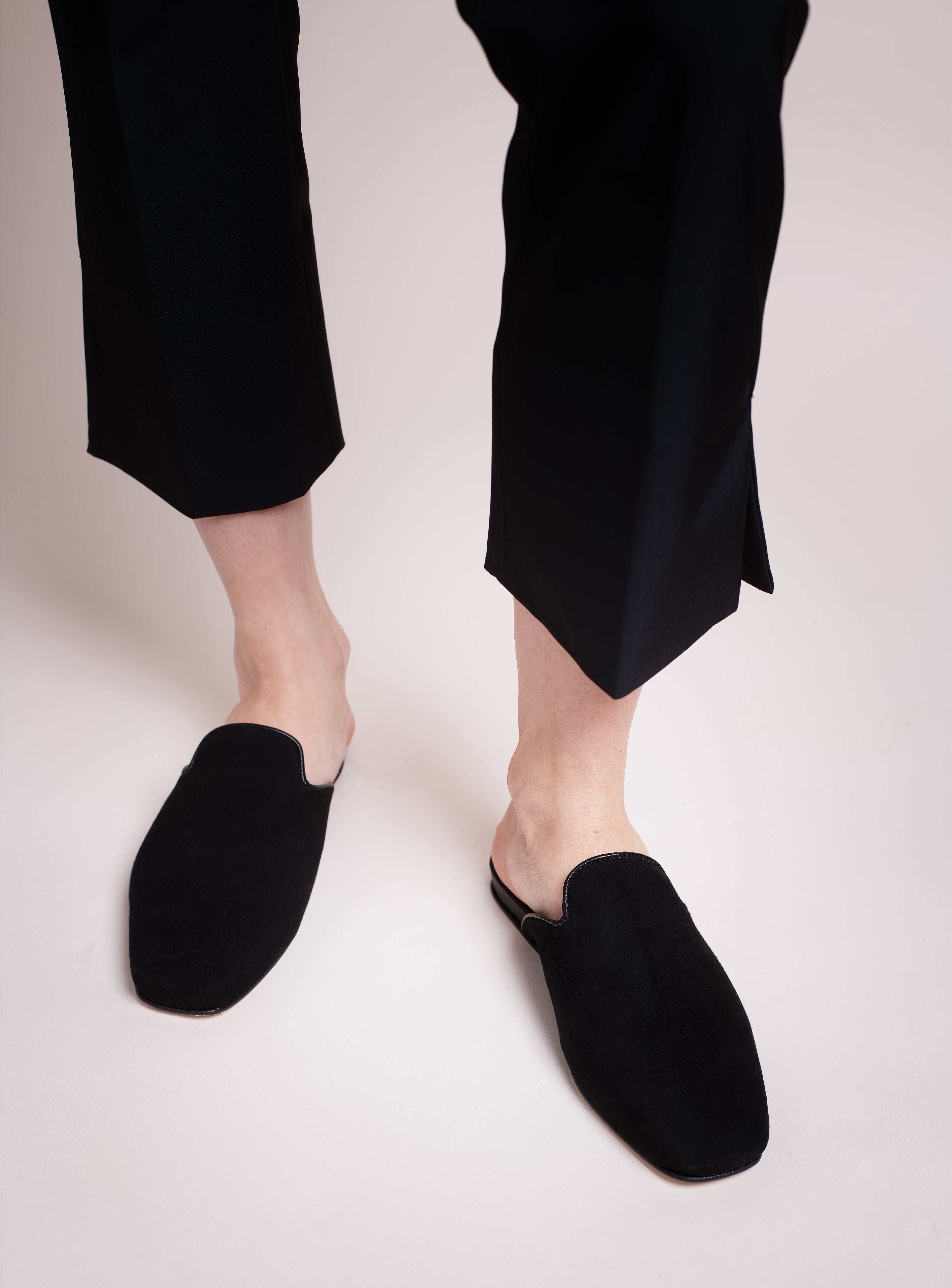 Woman wearing black suede slippers with black capri pants on light backdrop. 