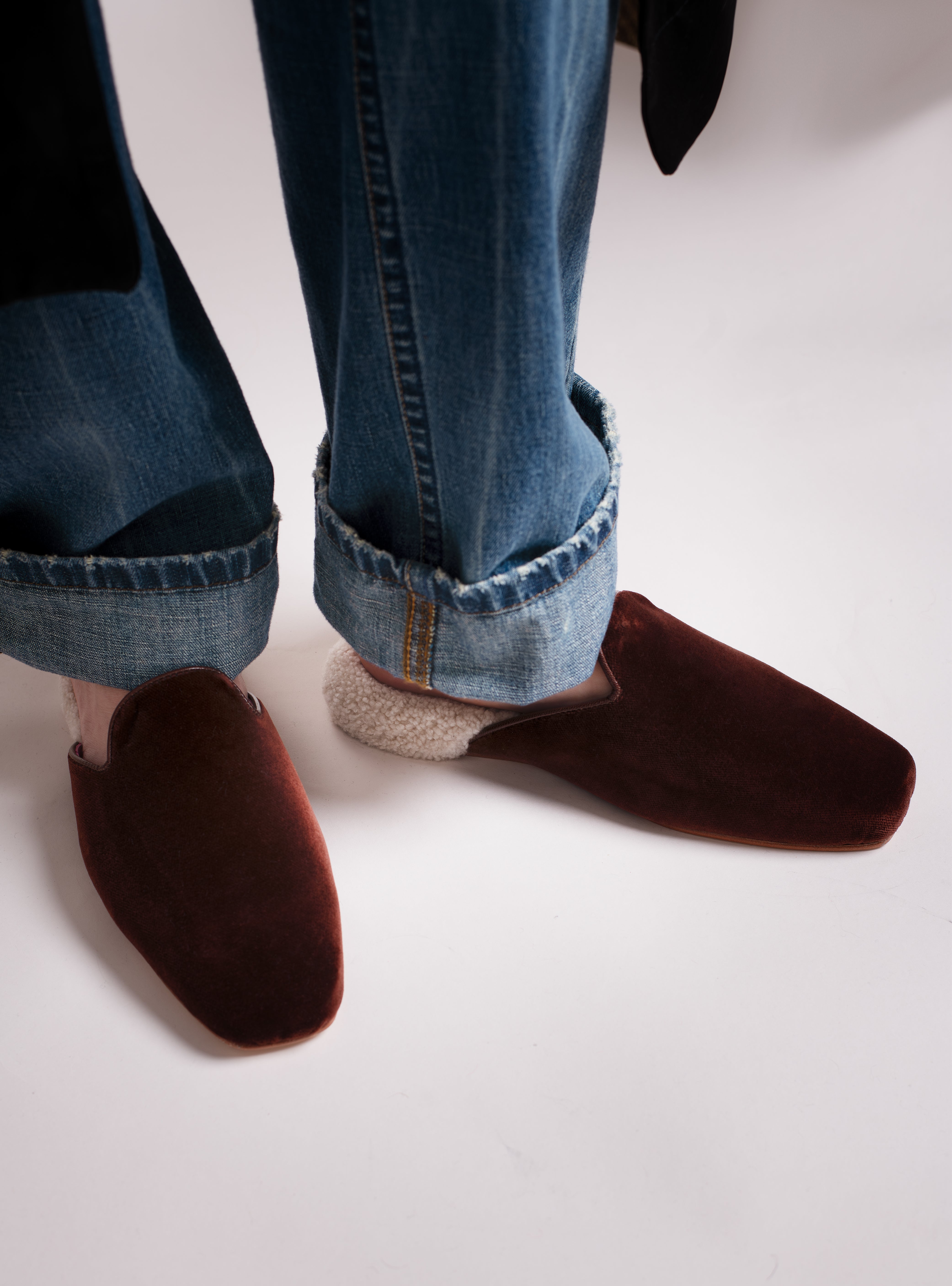 Women's Brown velvet slippers with white shearling worn with blue jeans on a white background