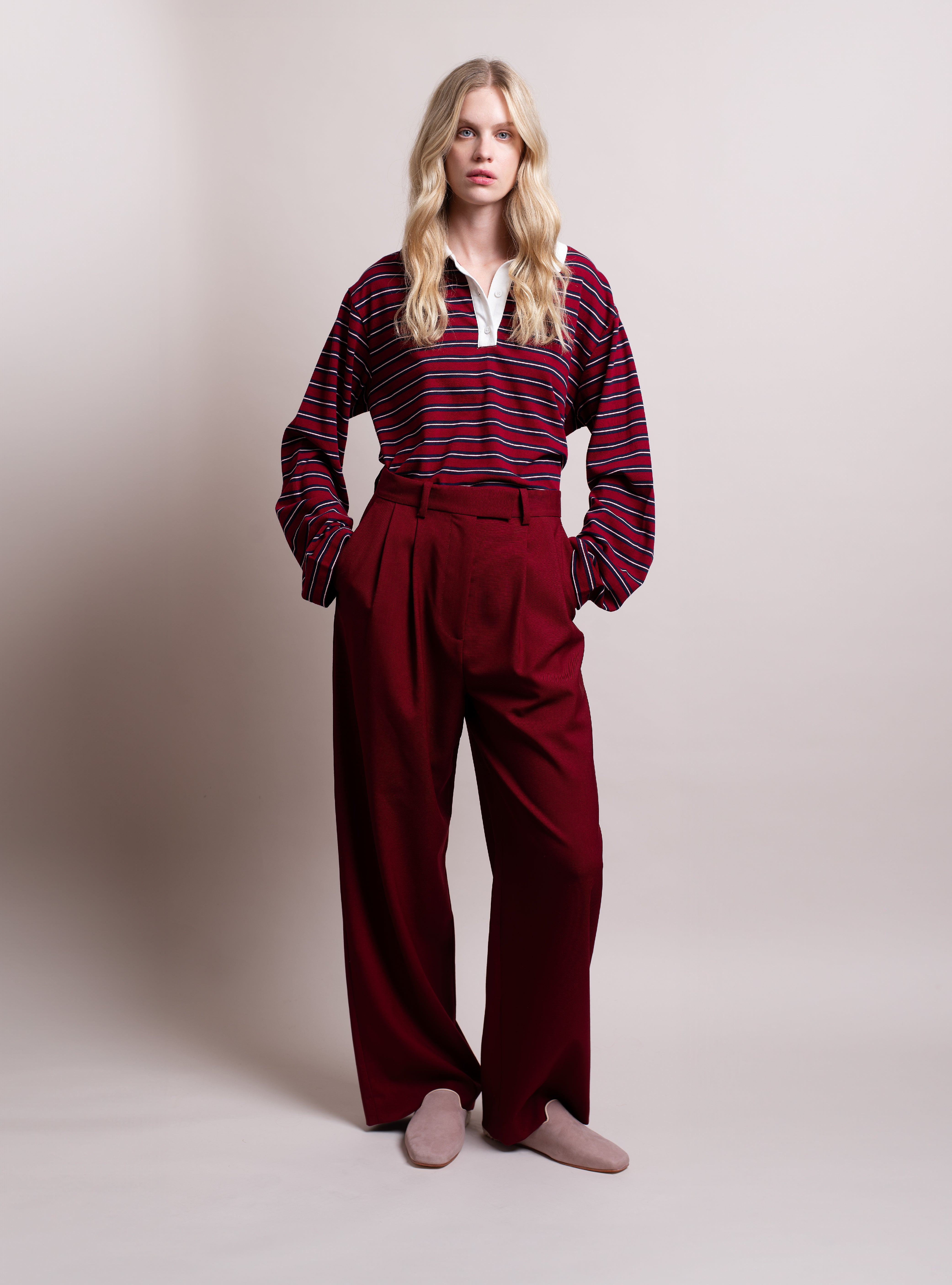Woman wearing a striped burgundy shirt, red pants, and pink suede slippers against a plain background.