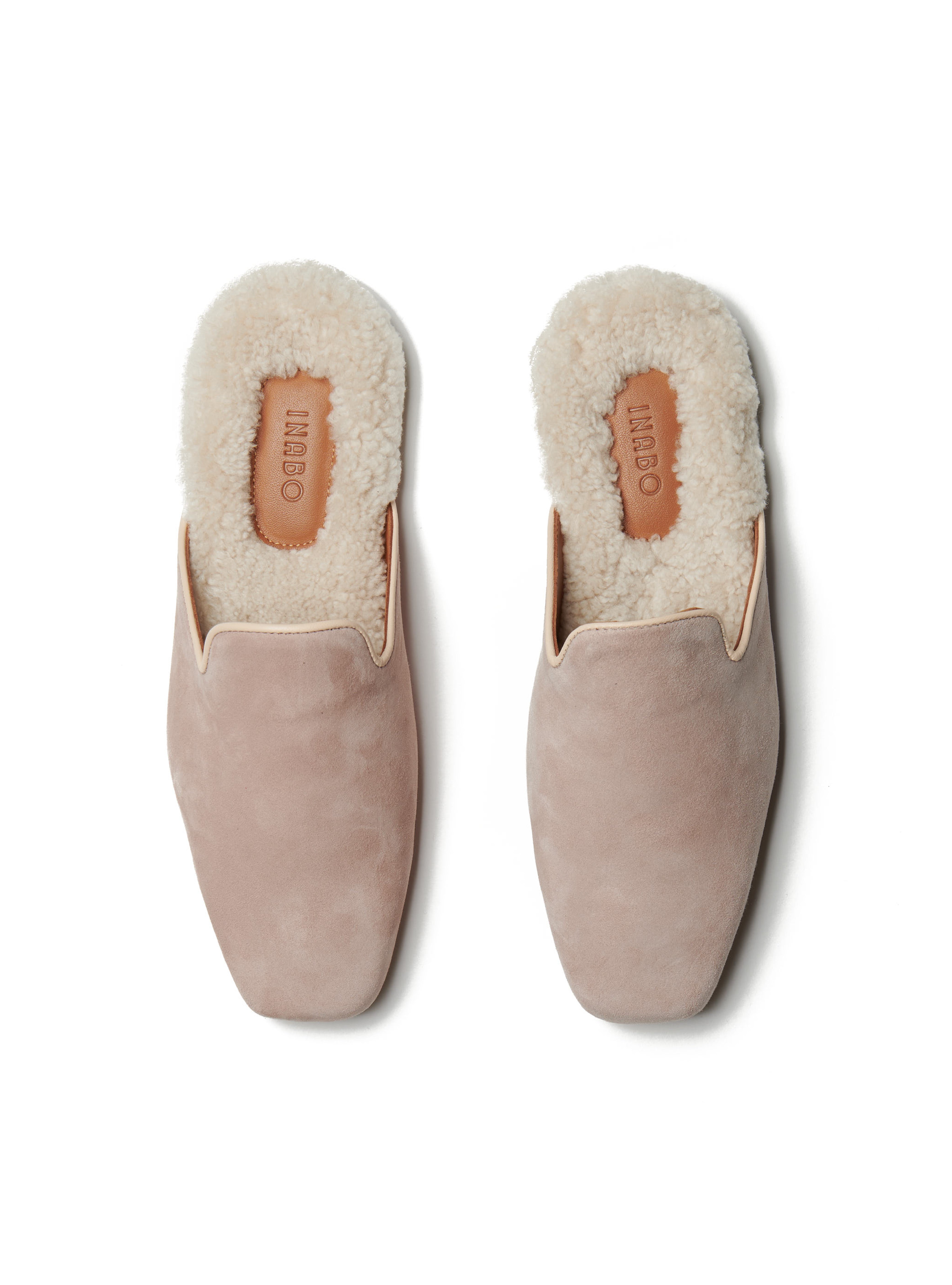 Women's pair of pink suede slippers with shearling lining on a white background