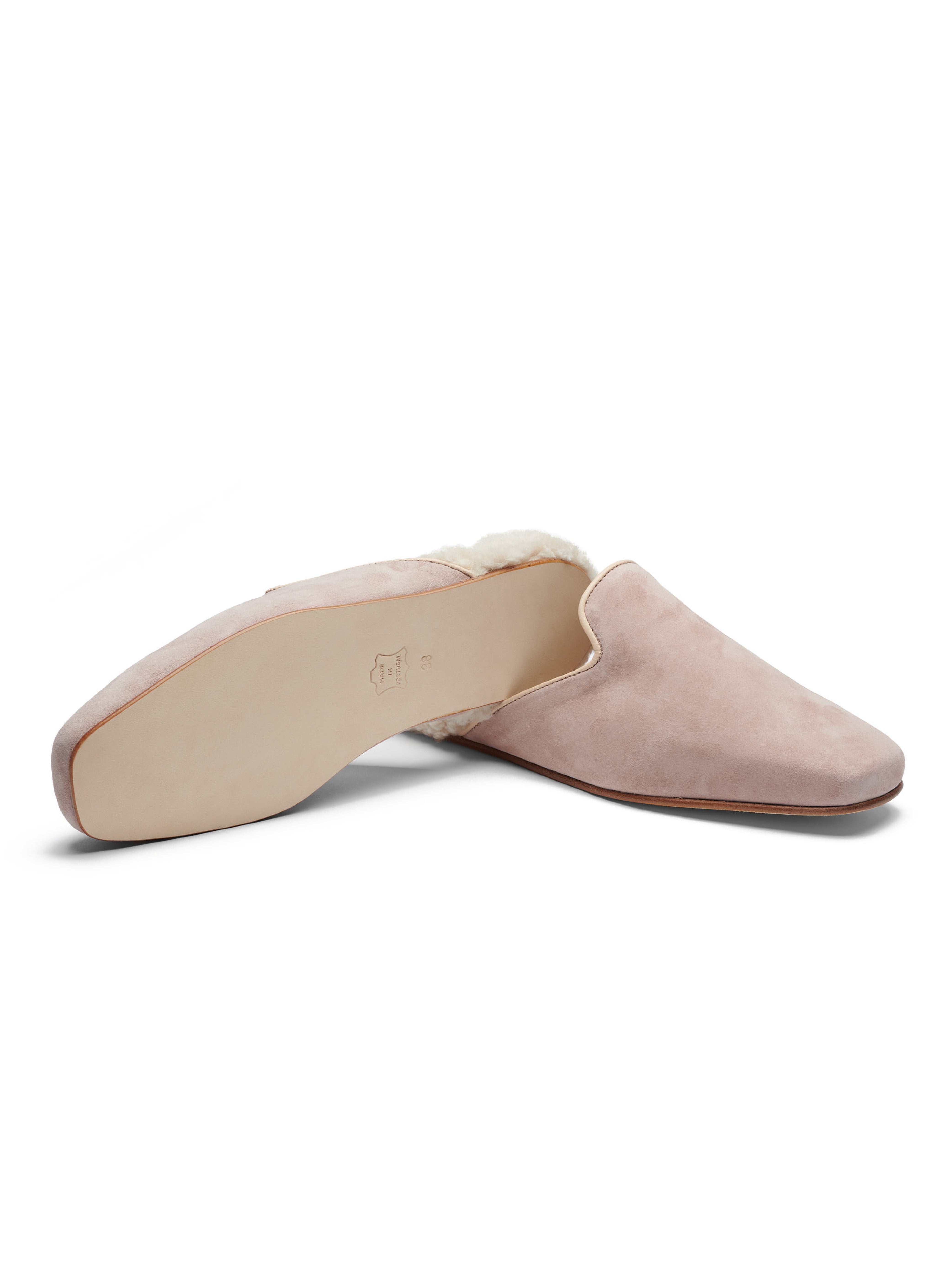 Women's pair of pink suede slippers with shearling lining and leather outsole on a white background