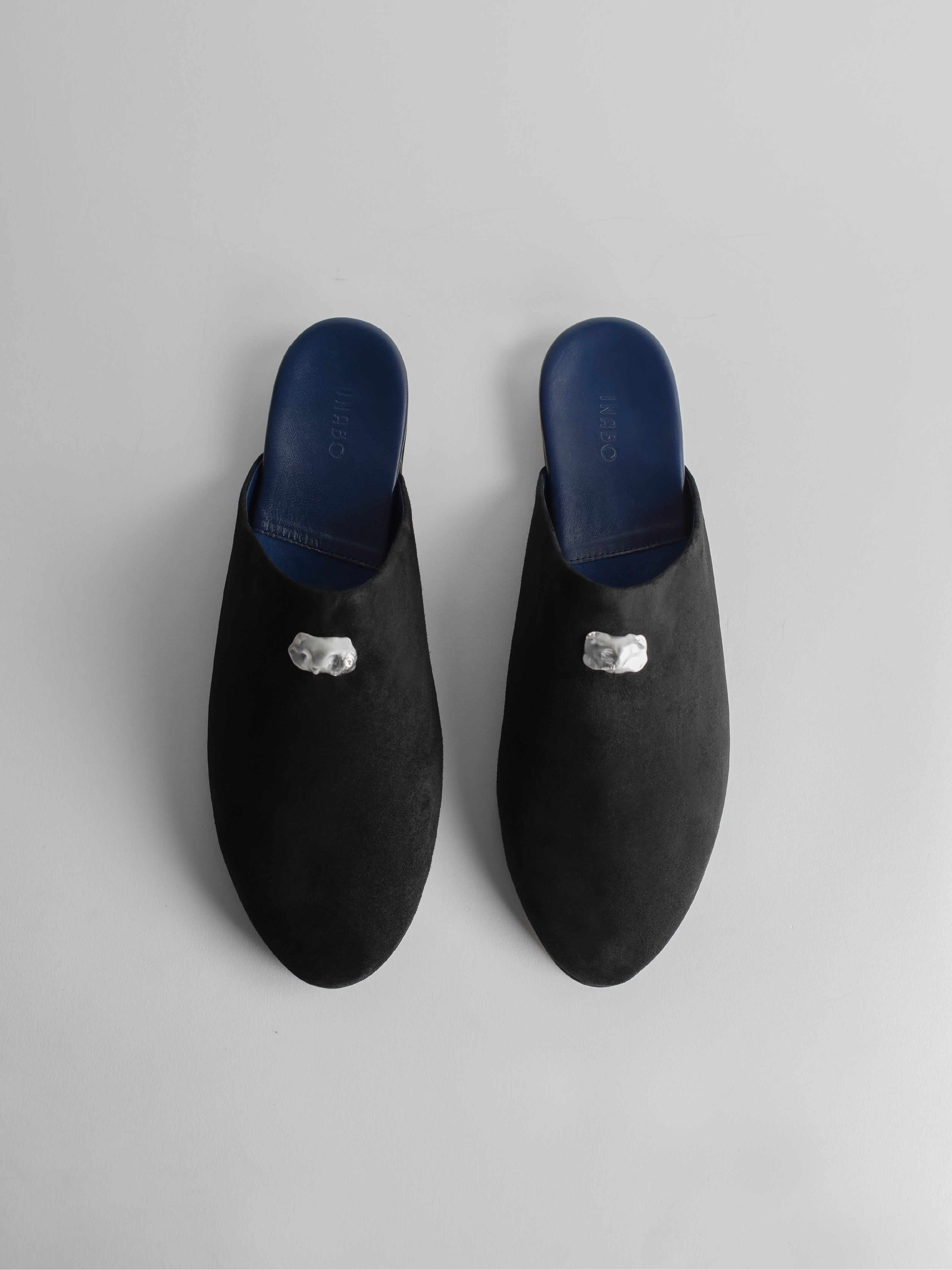 Men's pair of black slip-on house shoes decorated with sterling silver pieces on a light gray background