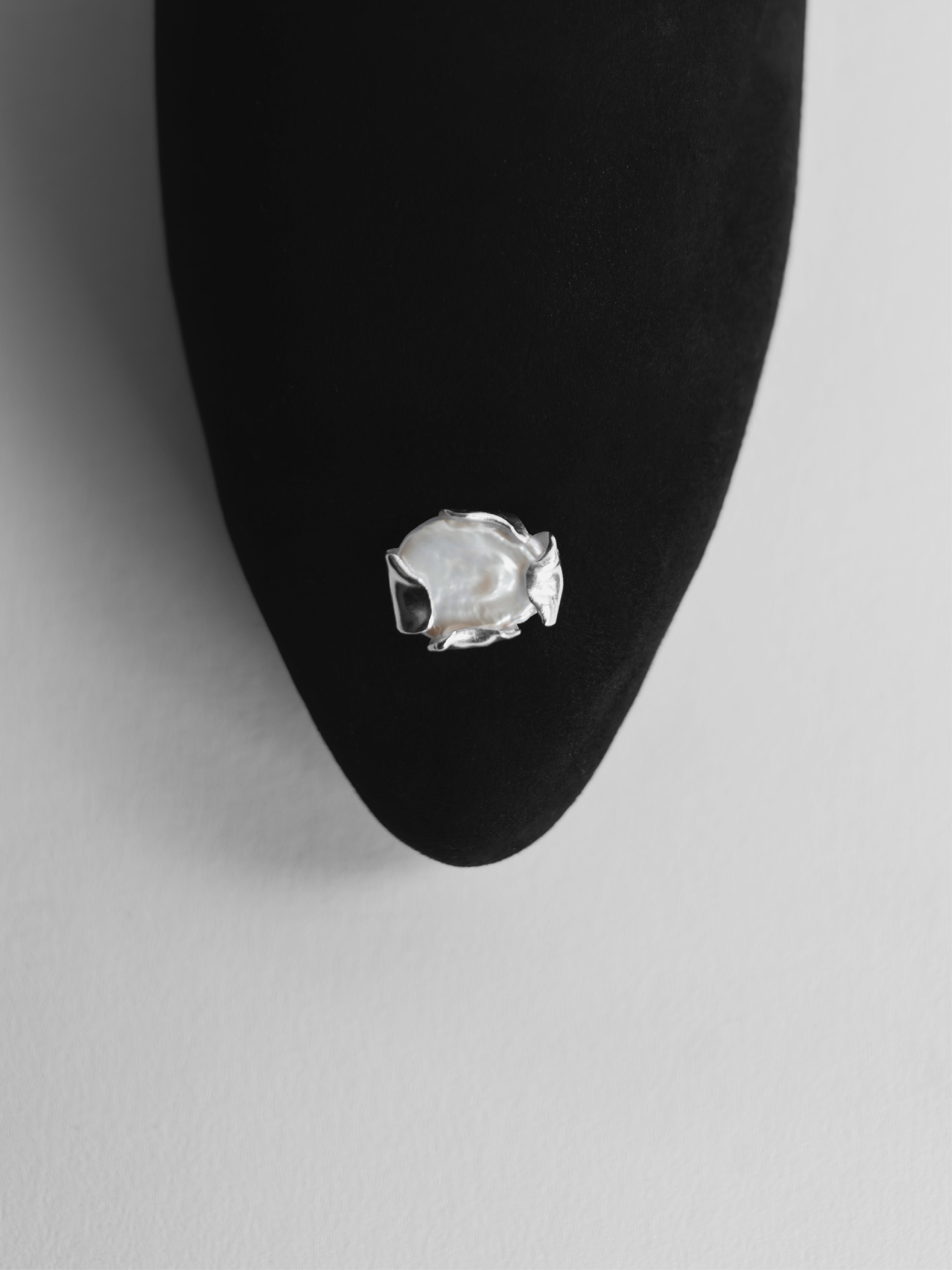 Silver and pearl jewelry attached on a black suede slipper with a gray background