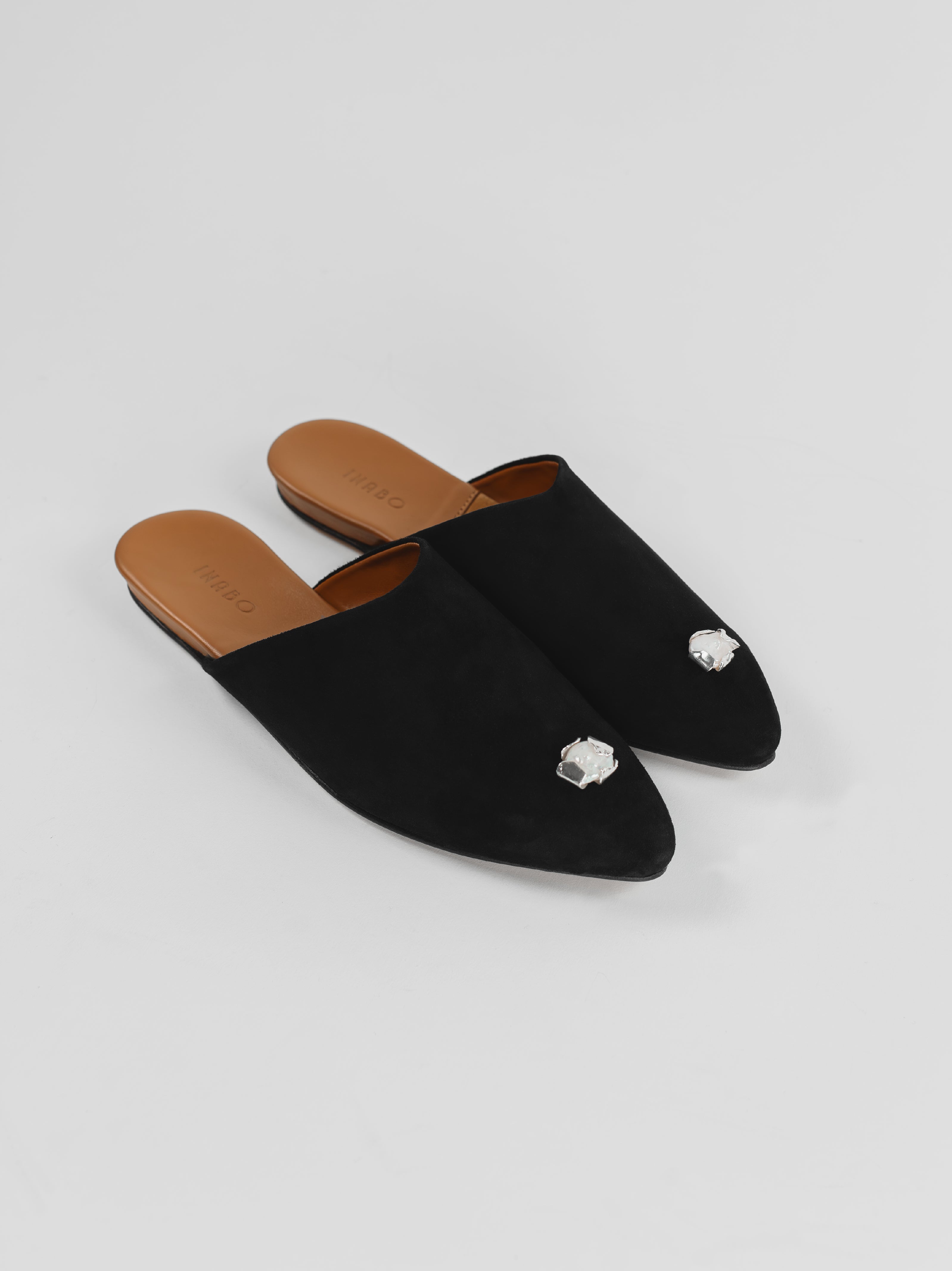 Black suede slippers with decorative silver jewelry on a light gray background