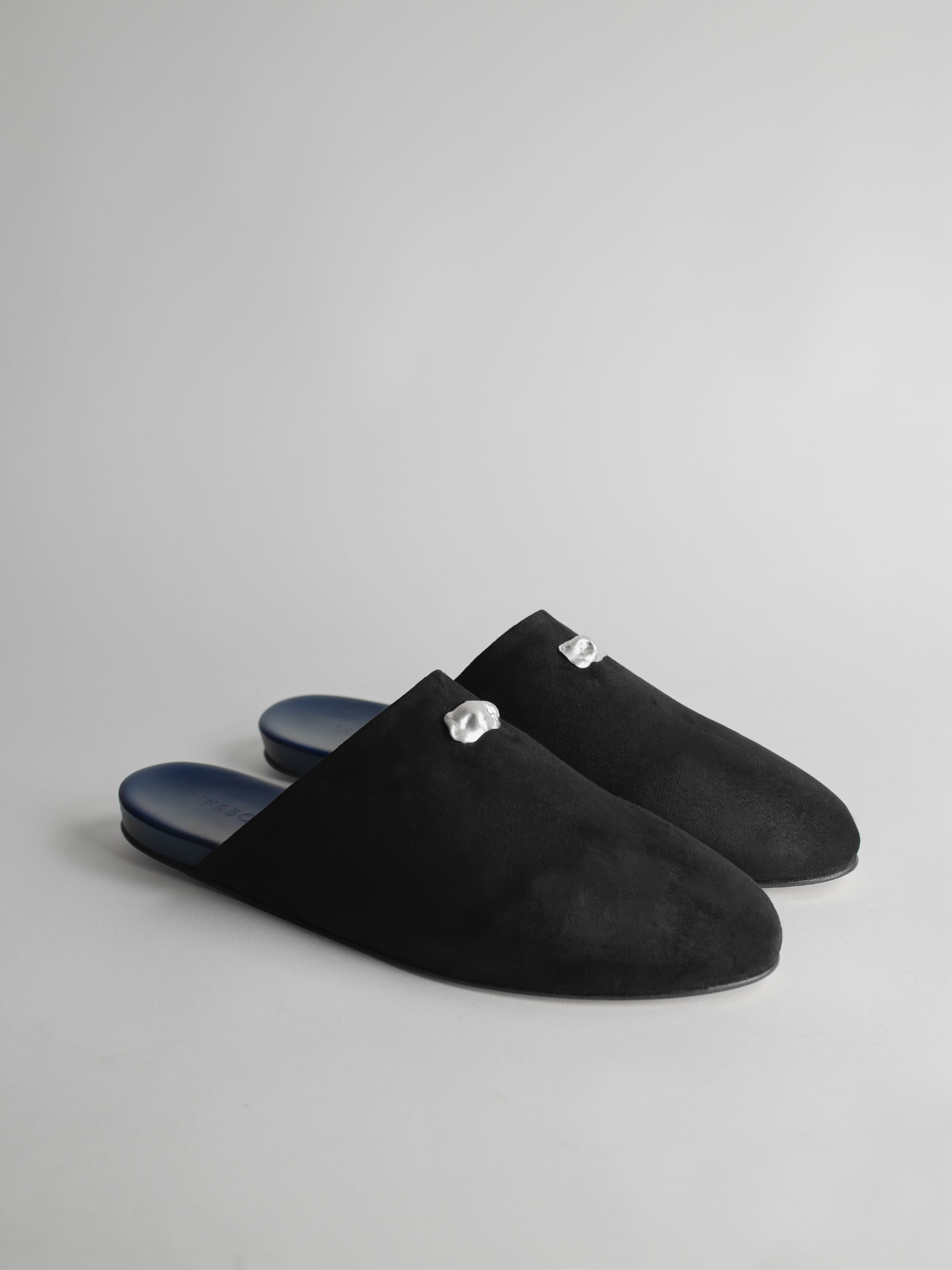 Men's pair of black suede slippers, decorated with sterling silver pieces, on a light gray background