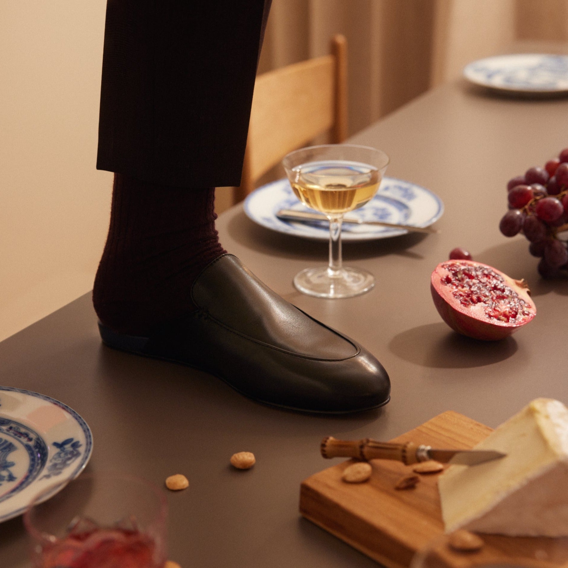 Inabo Men's Slofwer in Black leather worn by a man standing with one feet on a laid table  
